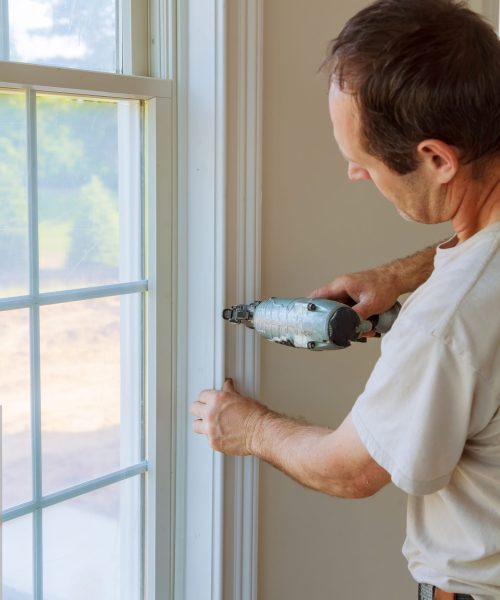 Carpenter brad using nail gun to moldings on windows, framing trim, with the warning label that all power tools have on them shown illustrating safety concept